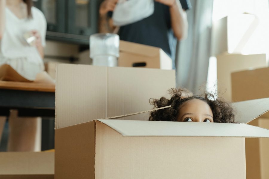 A child peeking out of a moving box while a family unpacks during a home move